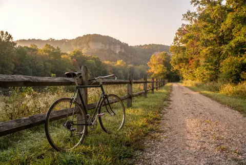 a bicycle against a fence beside a gravel rail trail in fall