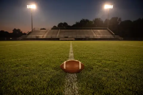 a football on a high school field under stadium lights